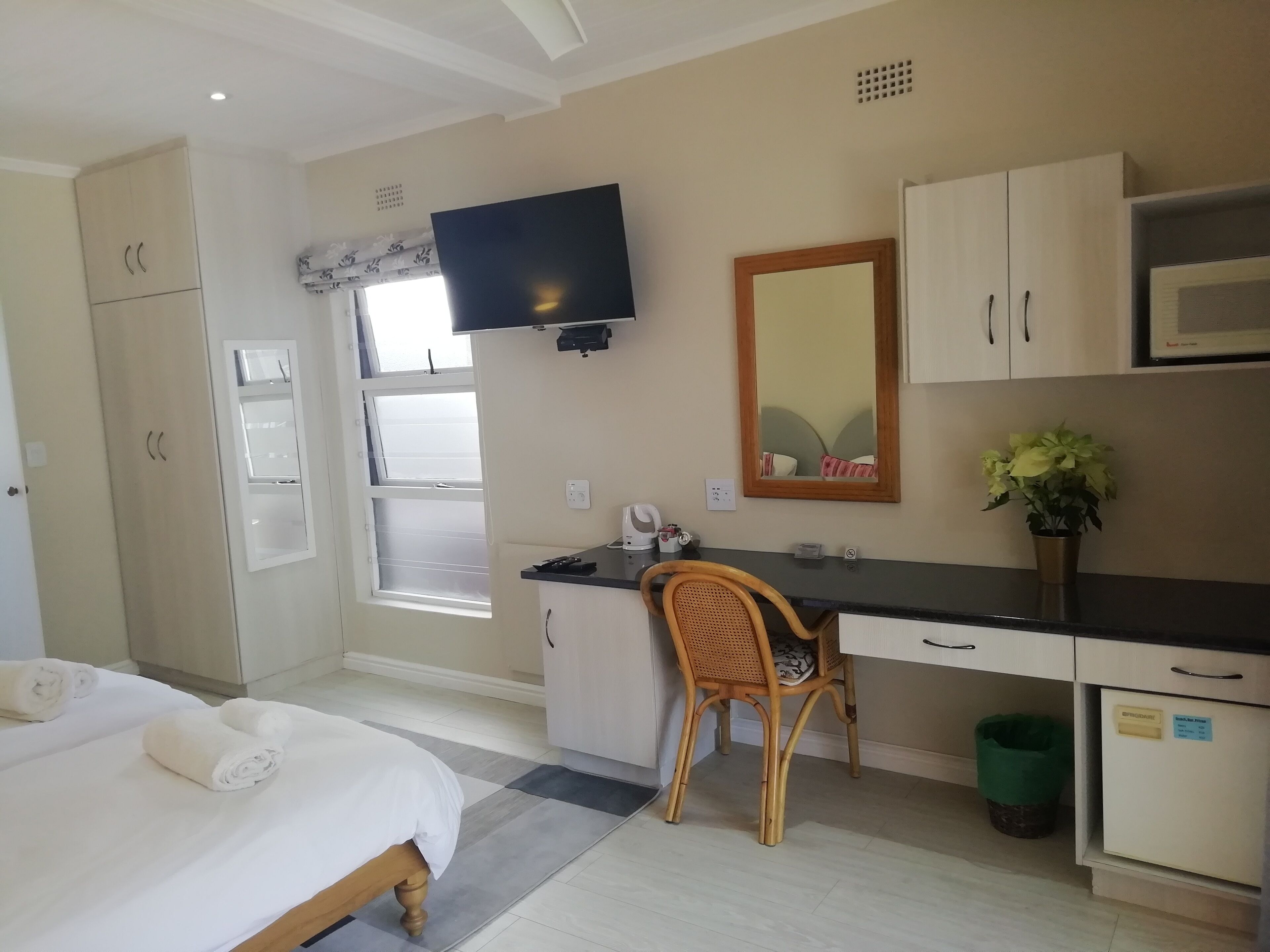 A hotel room with a bed, desk, chair, television, microwave, and a window.