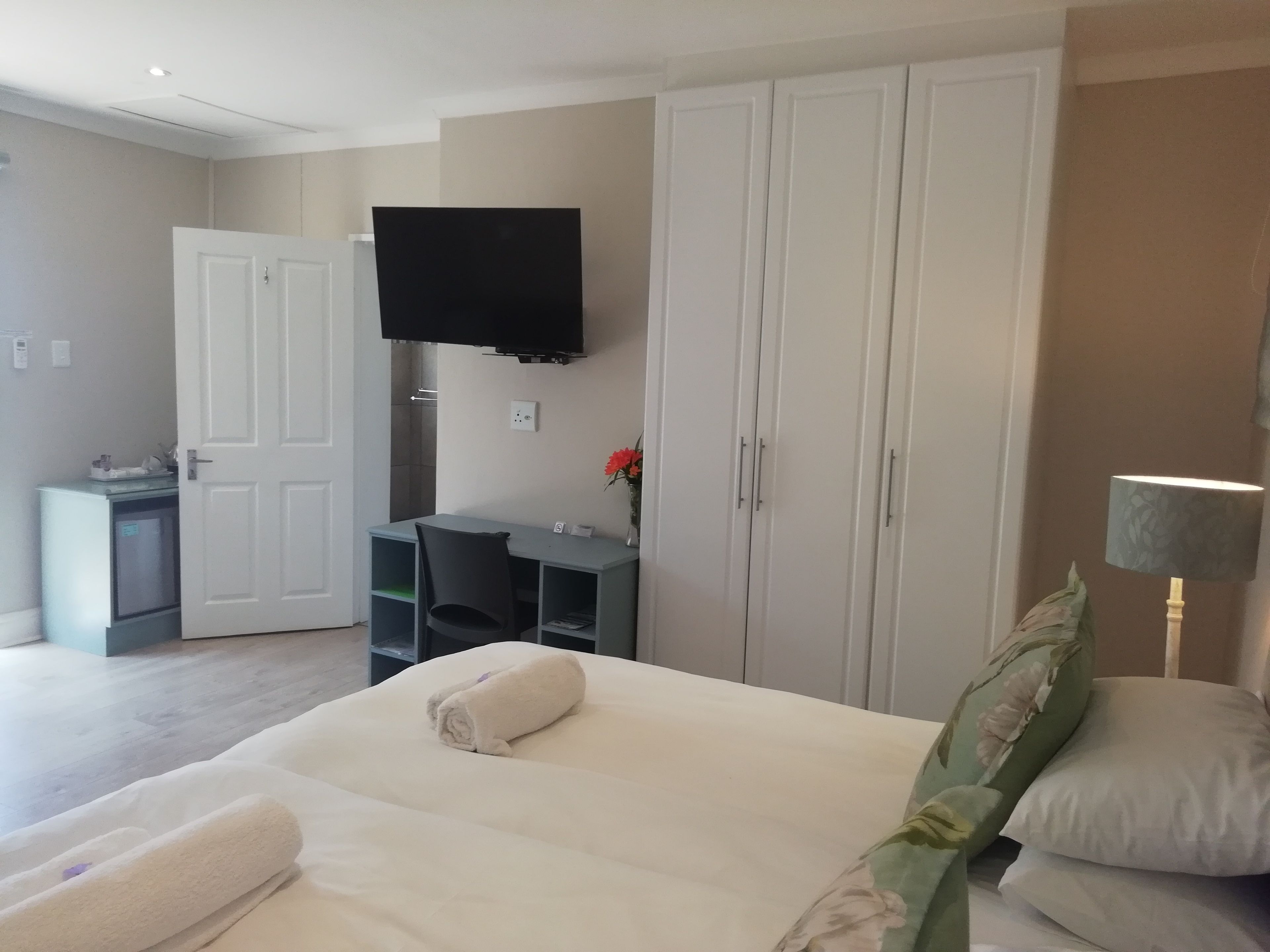 Quarto de hotel com cama, escrivaninha, televisão e guarda-roupa.