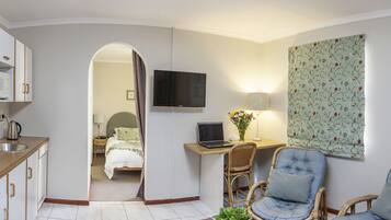 A compact room with a kitchenette, a bed, a desk with a laptop, and two chairs.