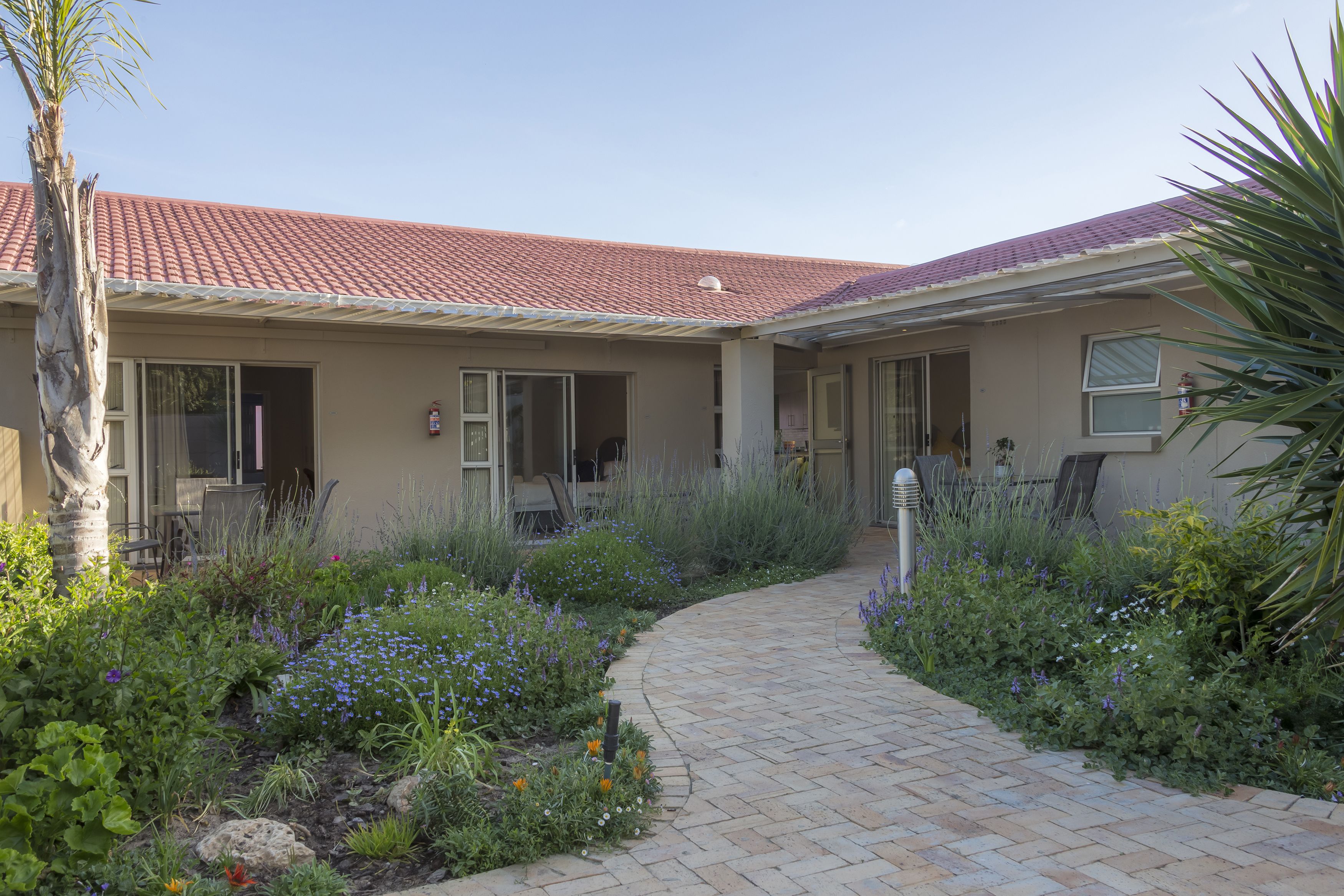 A house with a red-tiled roof, a brick pathway, and a garden with various plants and flowers.