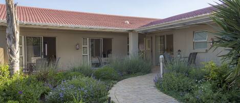 A house with a red-tiled roof, a brick pathway, and a garden with various plants and flowers.