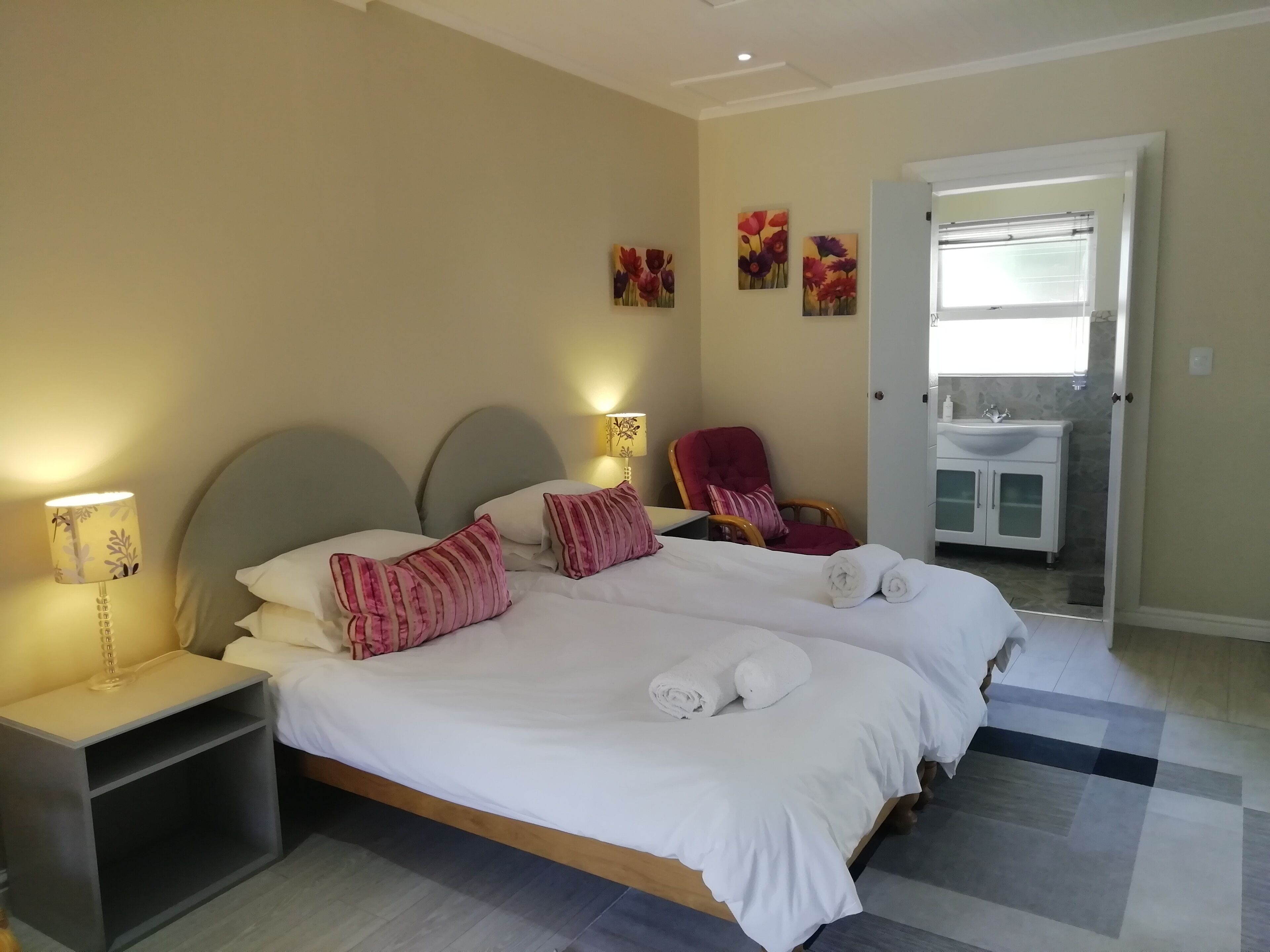A double bed with white linens and pink striped pillows, a nightstand with a lamp, and a red chair.