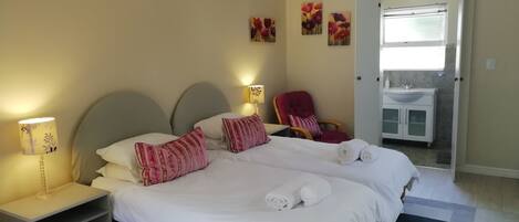 A double bed with white linens and pink striped pillows, a nightstand with a lamp, and a red chair.