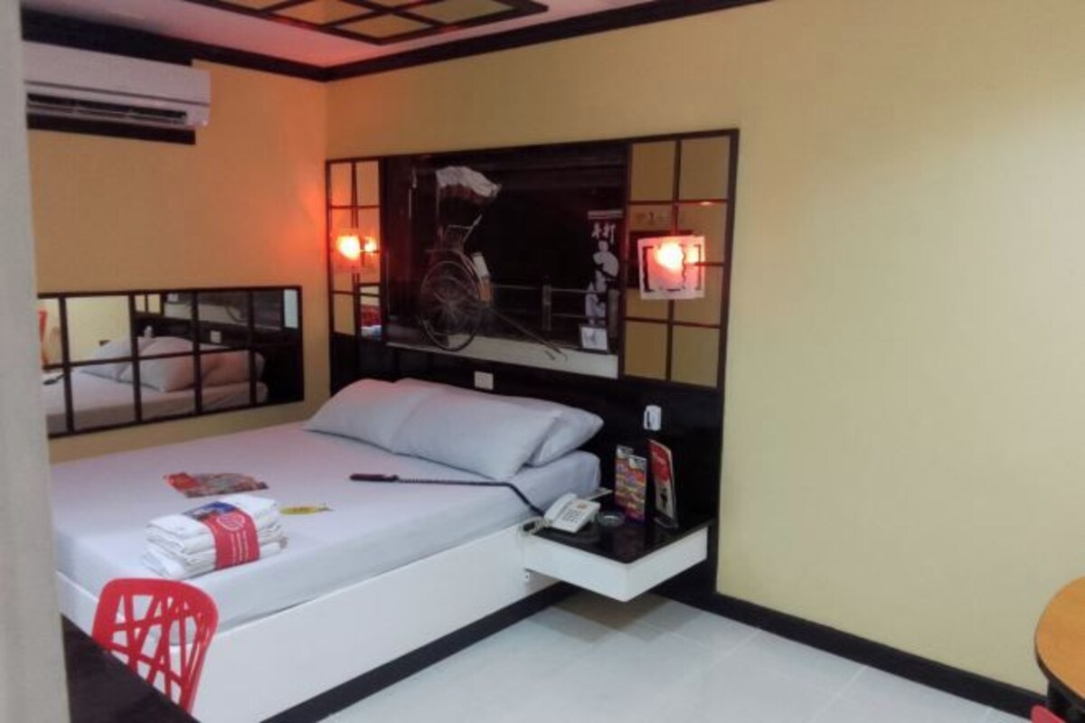 A compact hotel room with a single bed, a small table, a chair, and a wall-mounted TV.