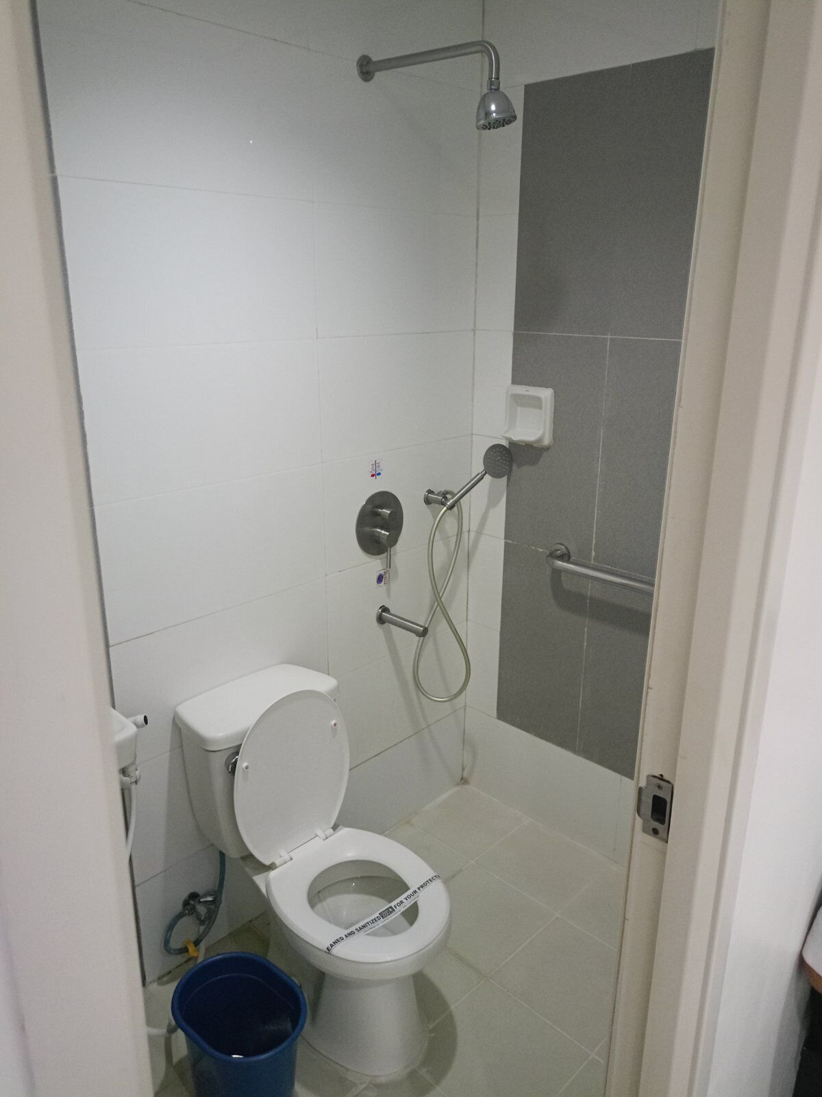 Un baño pequeño con inodoro, ducha y un cubo azul.