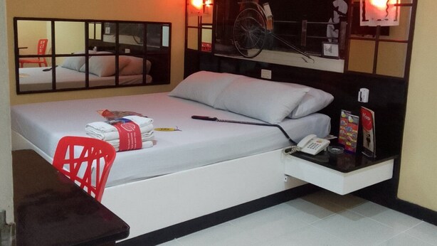 Habitación de hotel con cama, escritorio, silla, equipo de aire acondicionado y espejo.