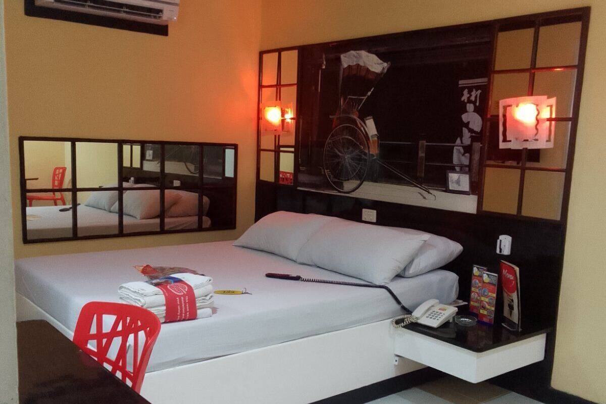 A hotel room with a bed, a desk, a chair, an air conditioning unit, and a mirror.