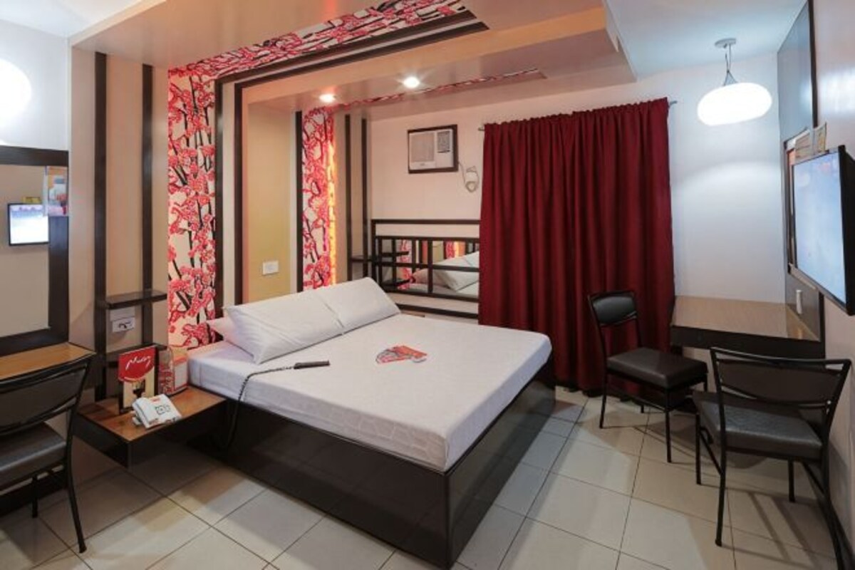 Una habitación de hotel con cama, escritorio, silla, televisión y una cortina roja.