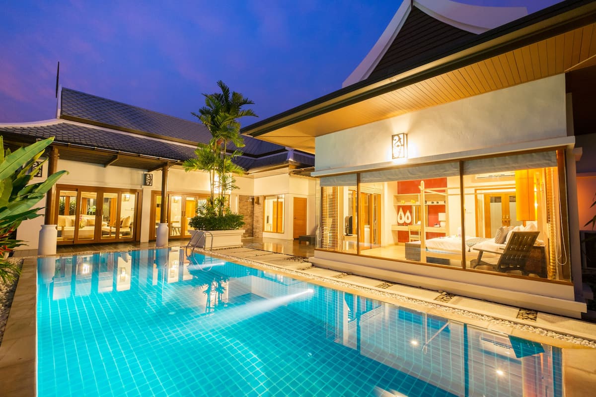 A swimming pool with a tiled deck, a building with a large glass window, and a palm tree.