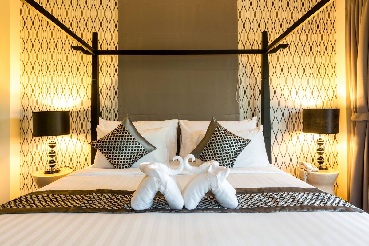 A hotel room with a four-poster bed, patterned wall decor, and two bedside lamps.