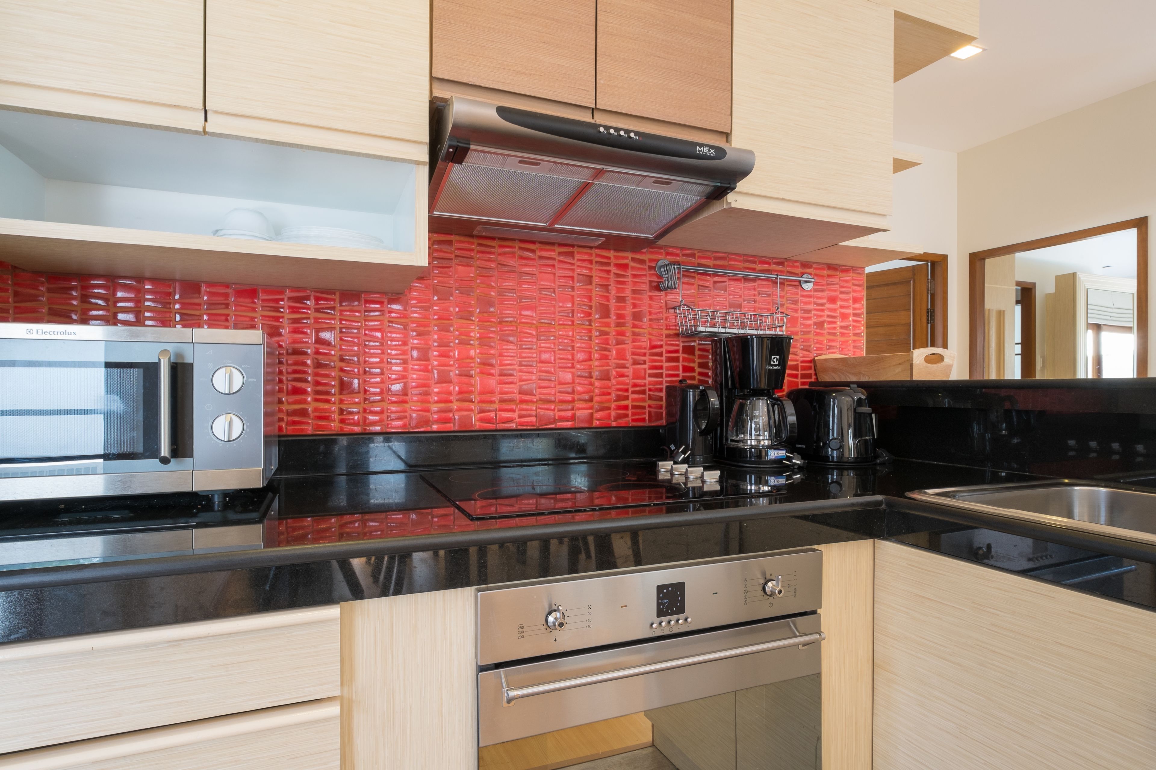 A modern kitchen with a stainless steel microwave, a black coffee maker, and a red-tiled backsplash.