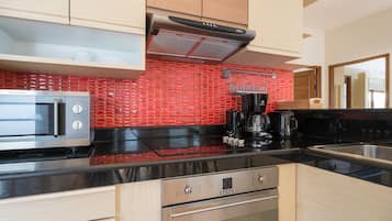 A modern kitchen with a stainless steel microwave, a black coffee maker, and a red-tiled backsplash.