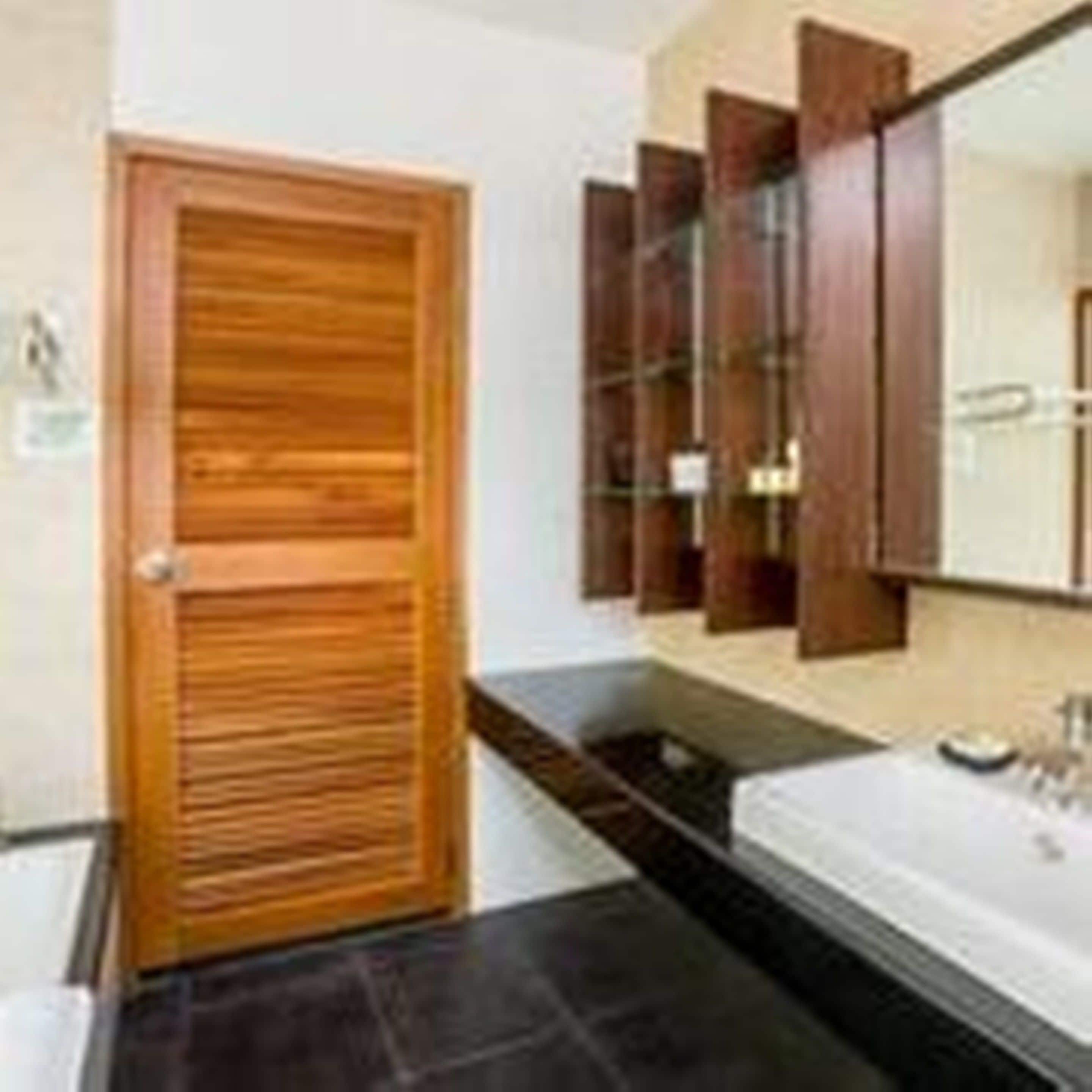 A bathroom with a wooden door, a sink, and a mirror with wooden cabinets above it.