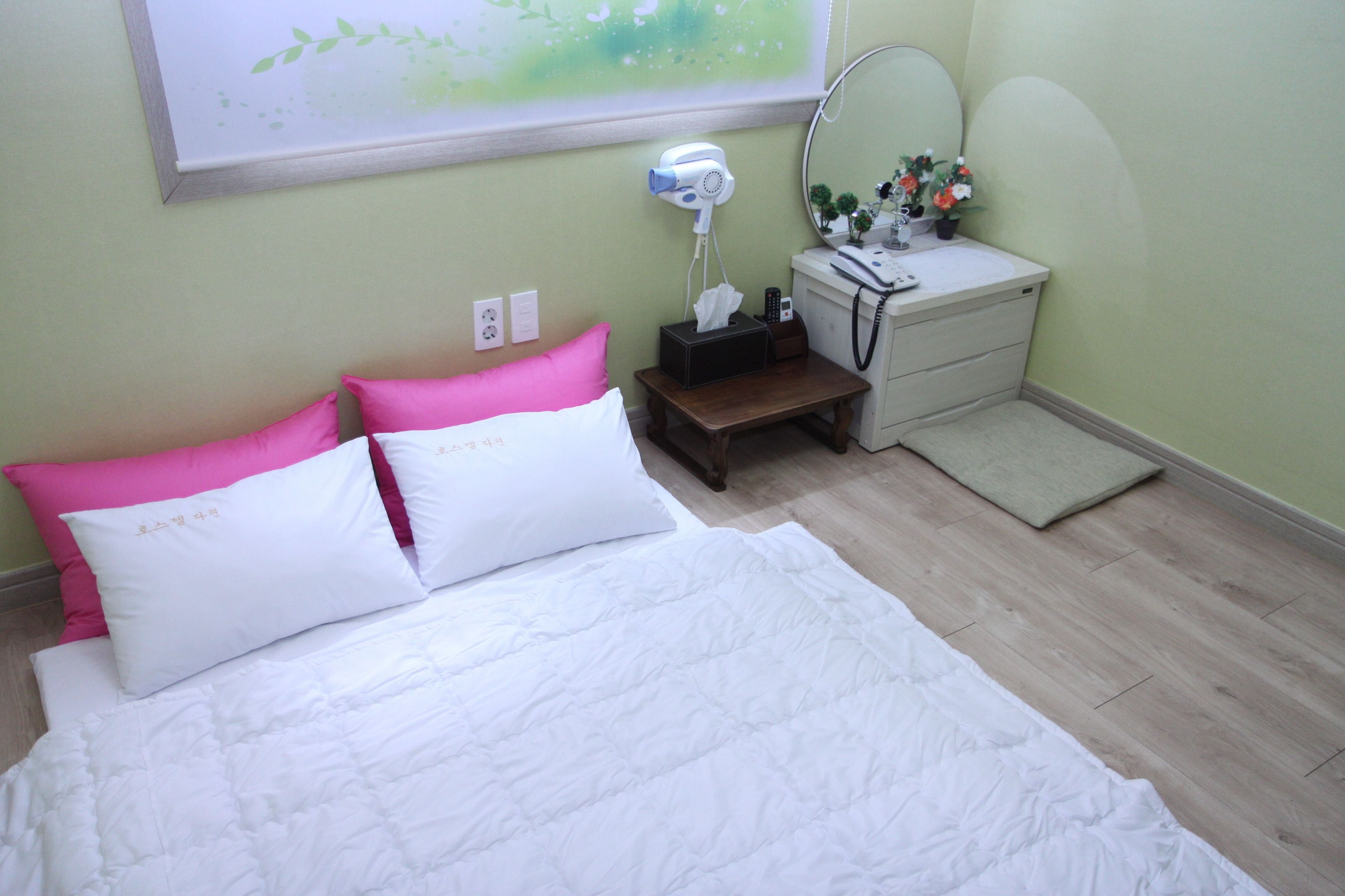 A bedroom with a bed, a bedside table with a lamp, a mirror, and a small plant.