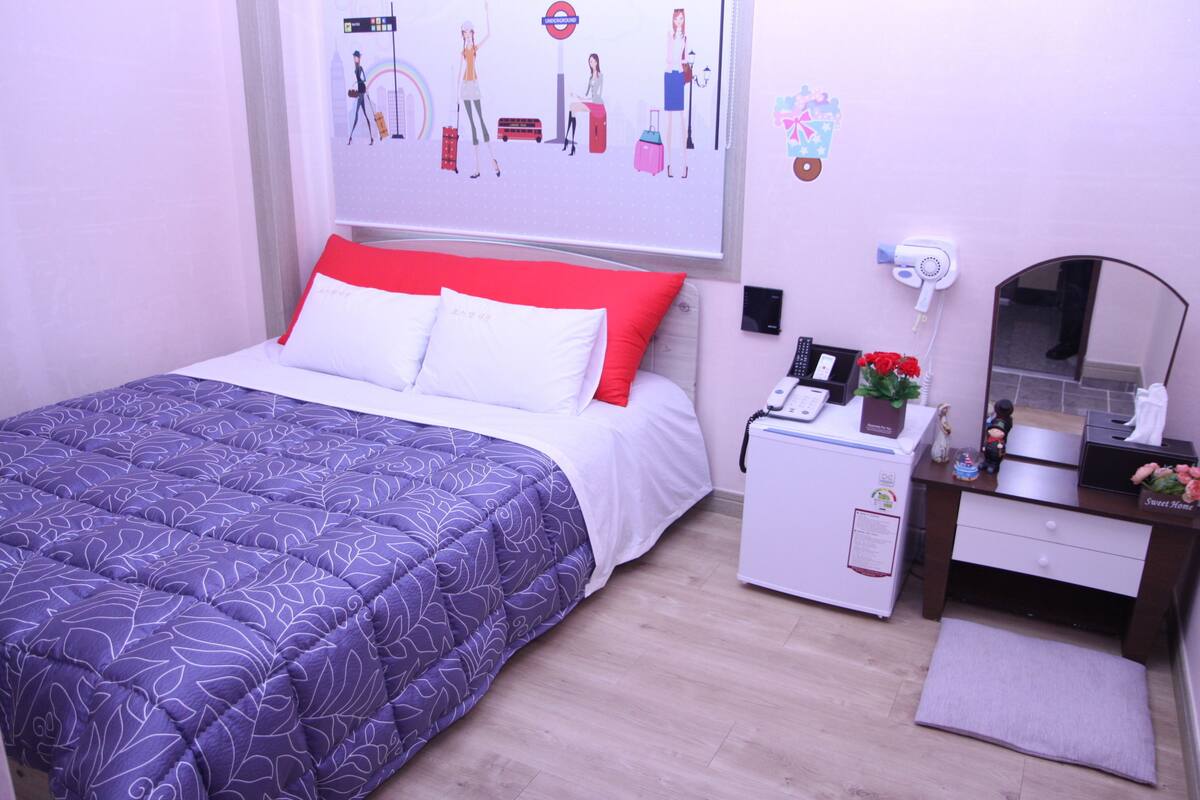 Ein ordentlich eingerichtetes Schlafzimmer mit einem Bett, einem Nachttisch mit Telefon und einer kleinen Pflanze, einem Schminktisch und einem Spiegel.