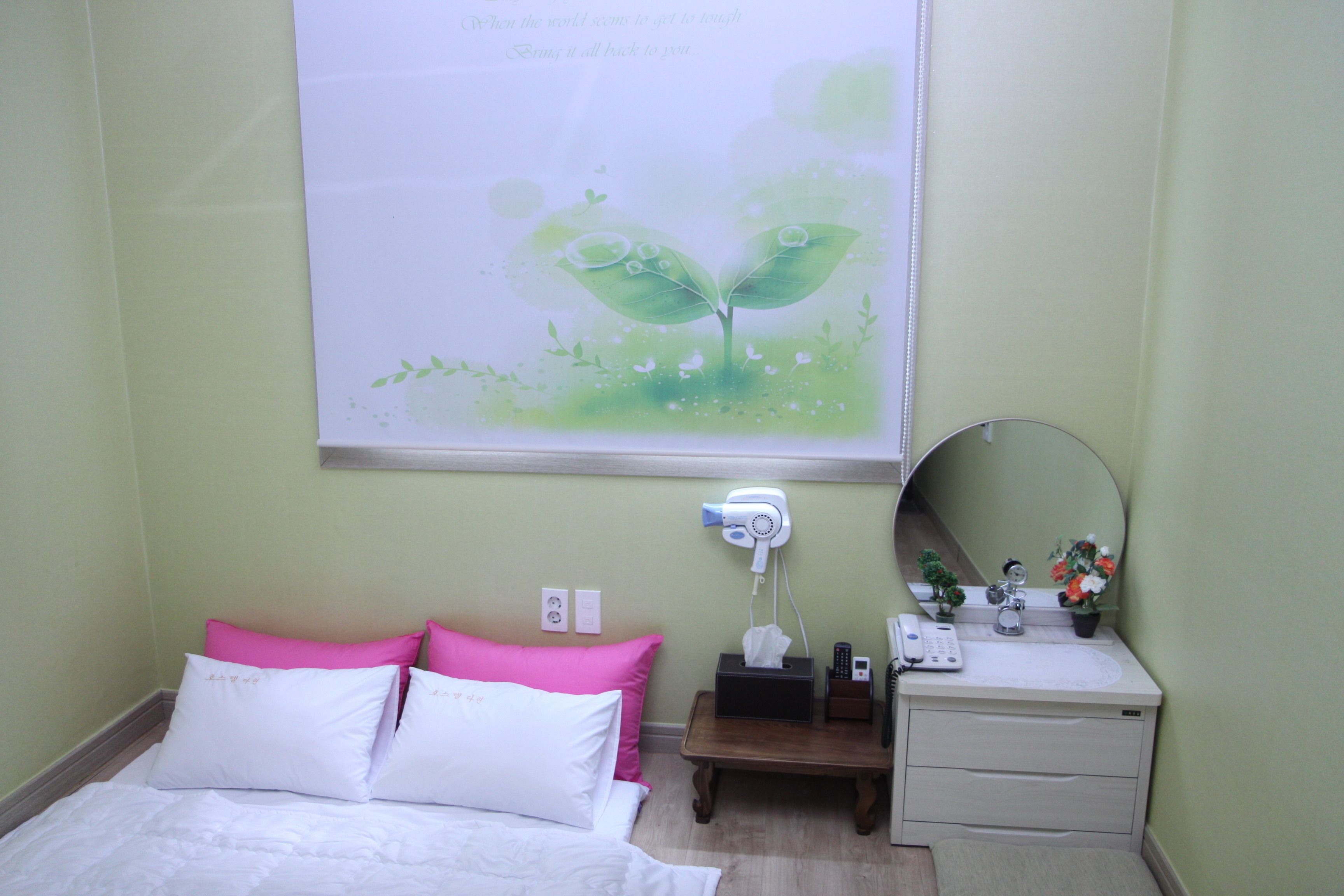 Une chambre d’hôtel comprenant un lit, une table de chevet, un miroir, un sèche-cheveux, un téléphone et une petite plante.