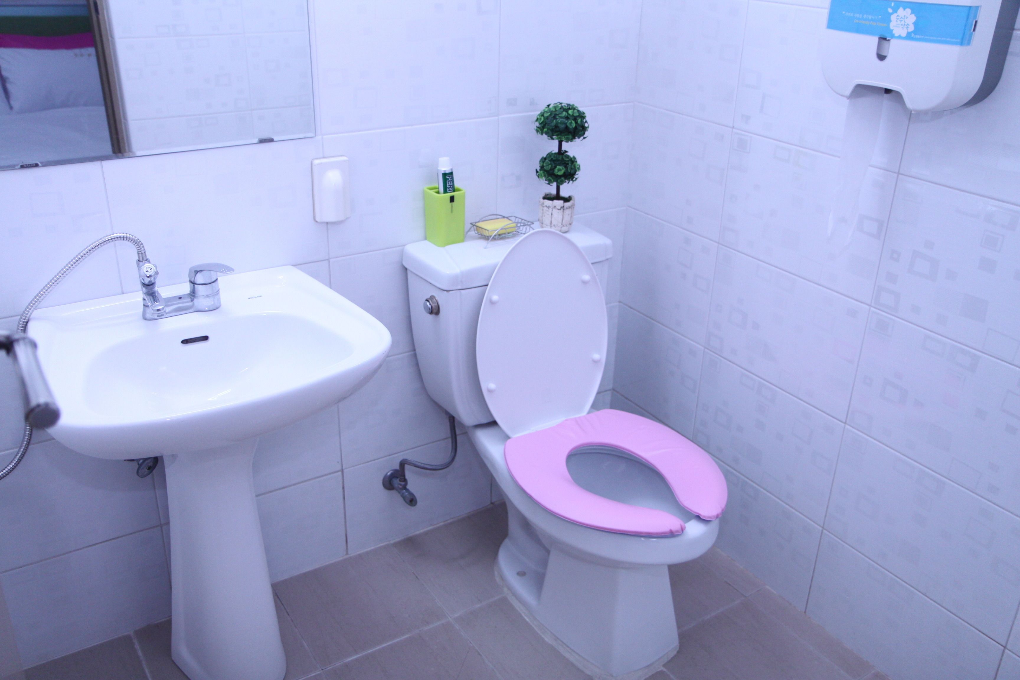 A bathroom with a white sink, a toilet with a pink seat, and a small potted plant on the back of the toilet.