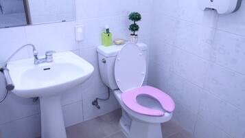 A bathroom with a white sink, a toilet with a pink seat, and a small potted plant on the back of the toilet.