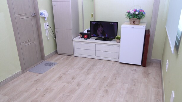 A small room with a wooden floor, a white cabinet, a television, a hairdryer, and a small plant. - Hostel Dahyun (Gyeongju)