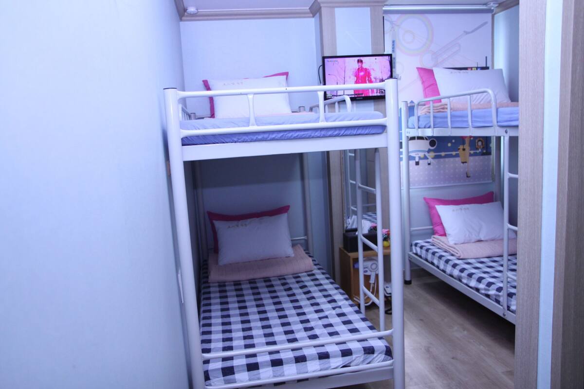 Ein Schlafsaalzimmer mit Etagenbetten, einem Schreibtisch, einem Stuhl, einem Fernseher und einem Fenster.