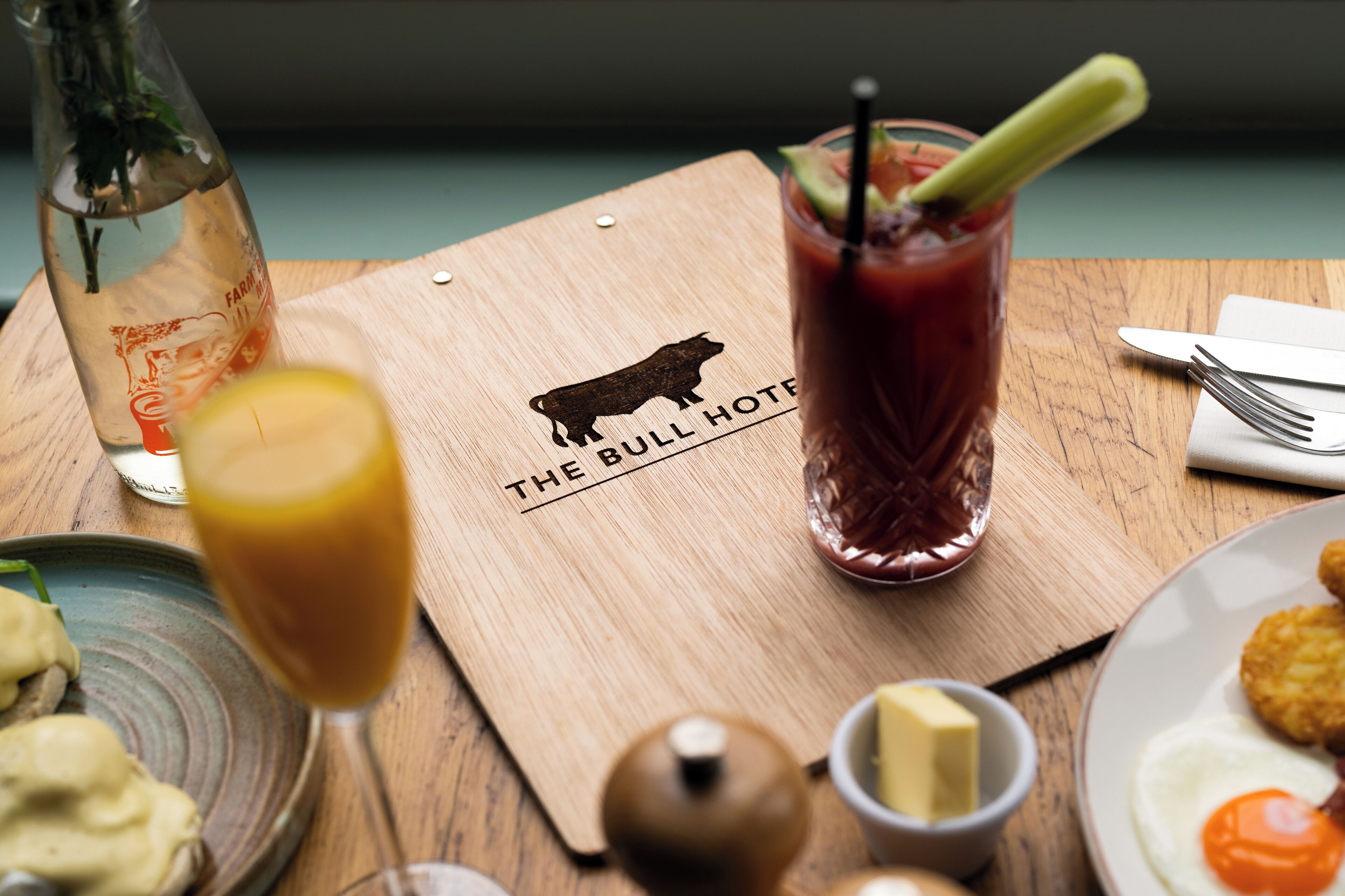 A wooden table with a glass of red drink, a bottle, and a plate with food.