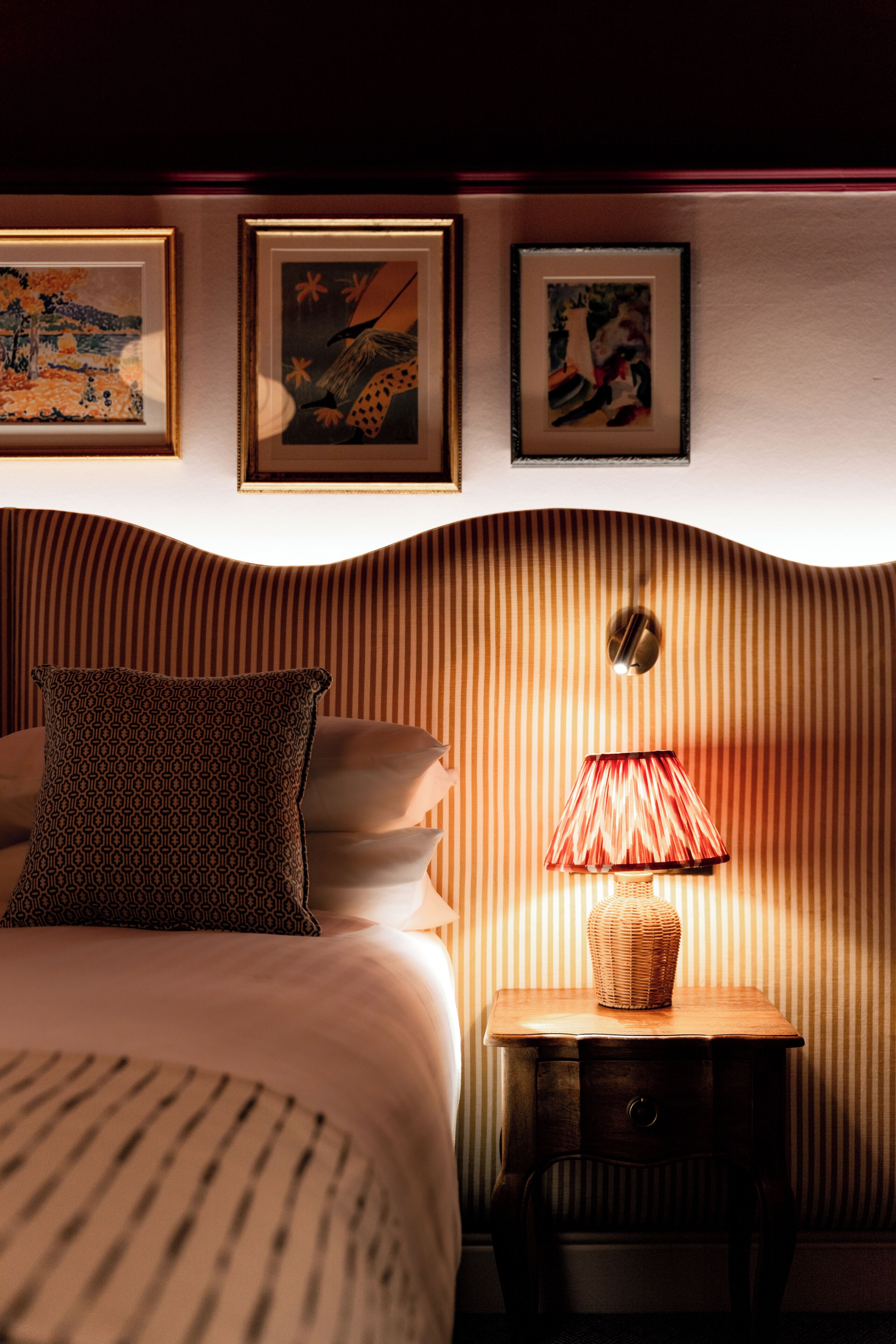 A hotel room with a bed, a nightstand with a lamp, and three framed pictures on the wall.
