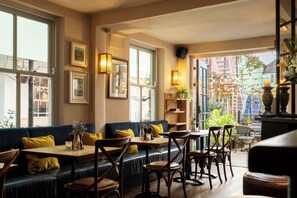 A cozy restaurant interior with a blue sofa, wooden tables, and chairs, and large windows offering a view of the city. - The Bull Hotel (Bridport)