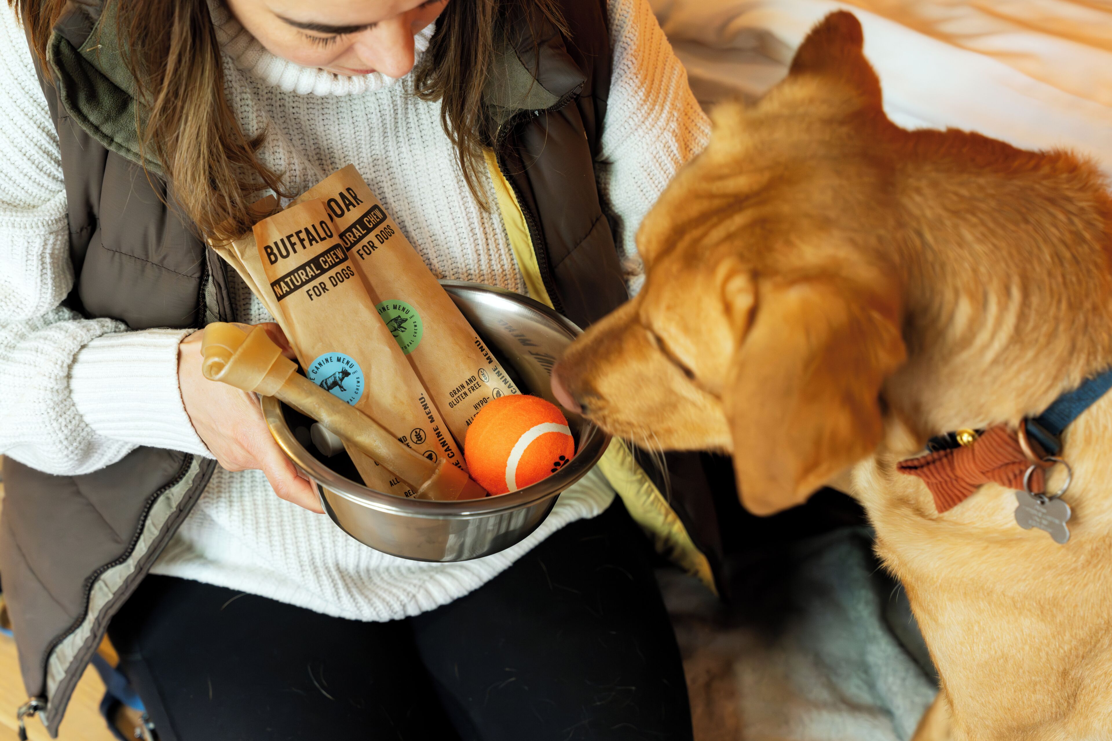 A person holding a bowl with a dog and a bag of dog food.