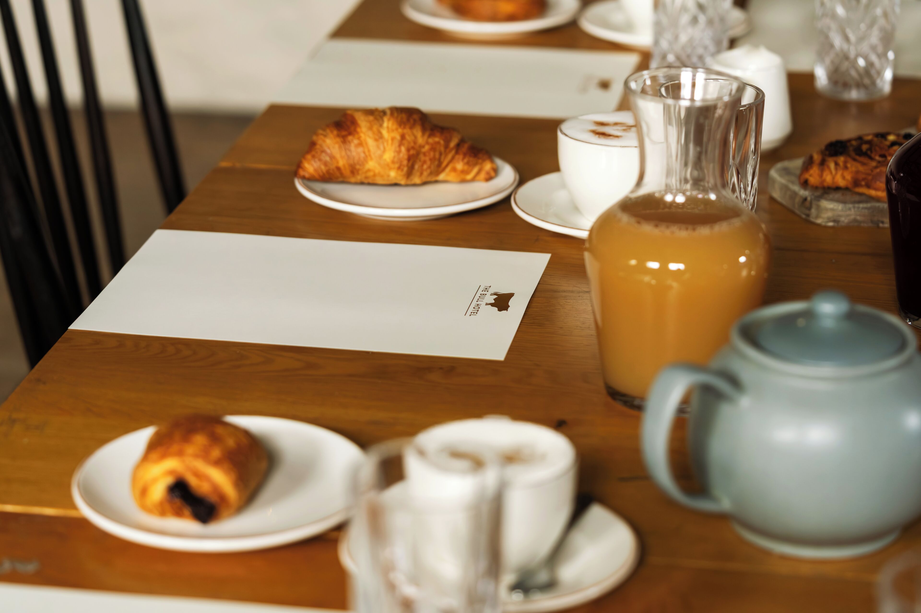 A breakfast table with croissants, a pitcher of orange juice, a teapot, and a menu.