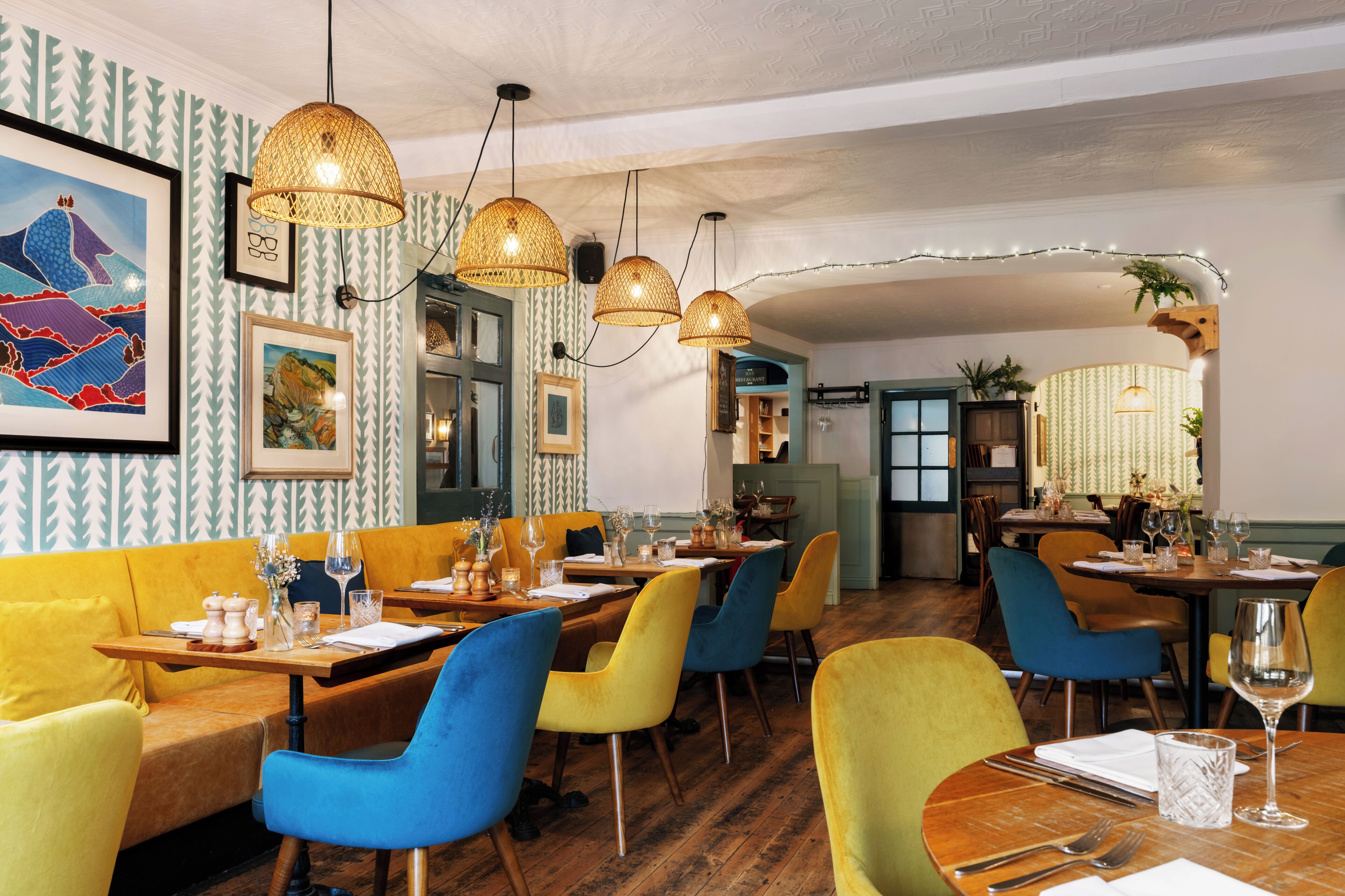 A restaurant with wooden tables, colorful chairs, and hanging lamps.