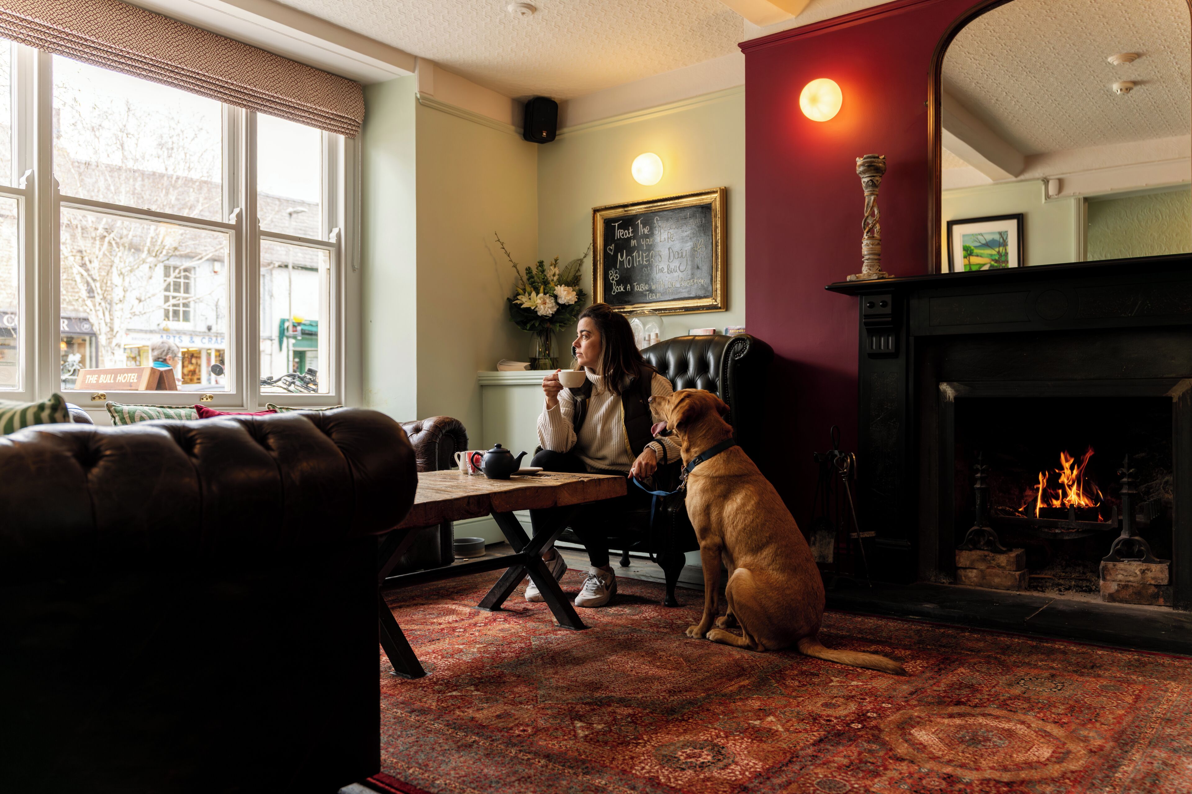 Ein gemütliches Wohnzimmer mit Kamin, einem Hund und einer Person, die an einem Tisch sitzt.