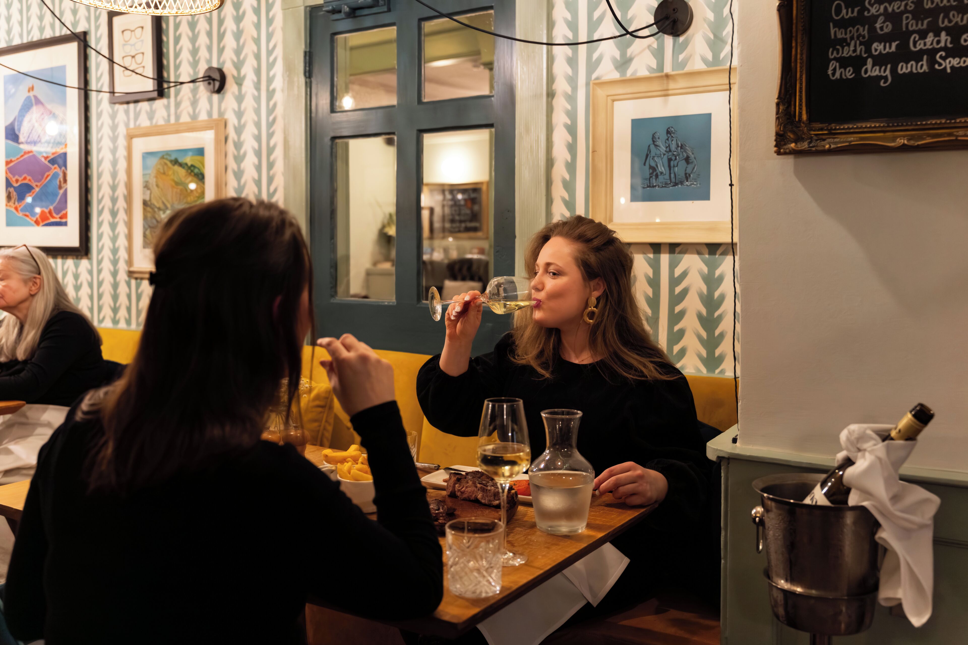 A dining area with a table, chairs, a bottle of champagne, and a framed picture on the wall.