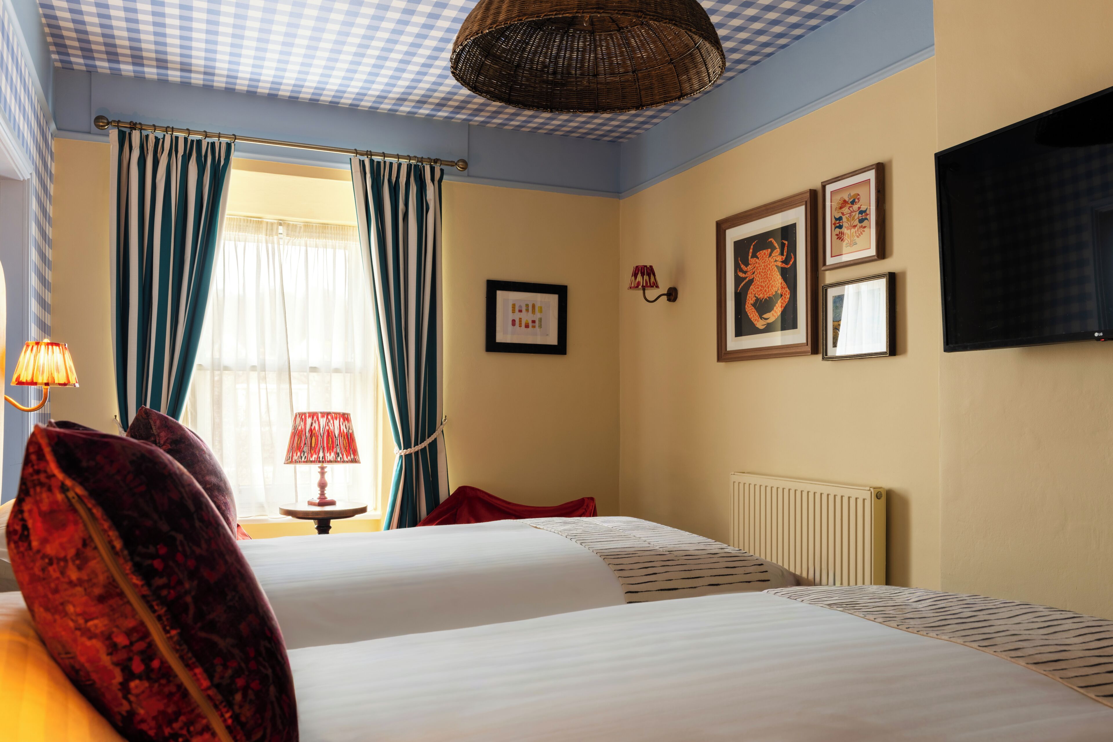 A hotel room with two beds, a window with curtains, a wall-mounted TV, and framed pictures.