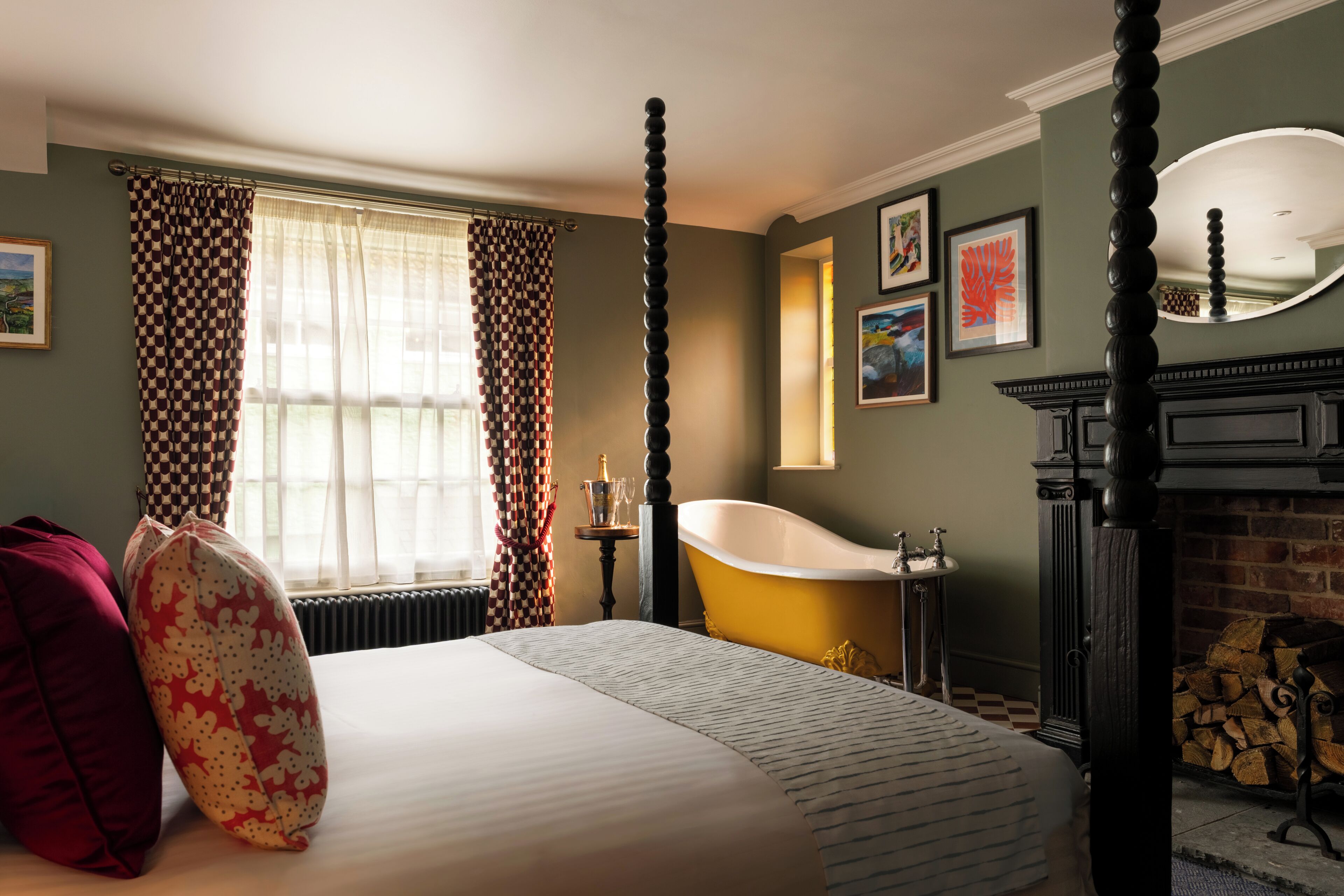 A bedroom with a large bed, a bathtub, a fireplace, and artwork on the walls.