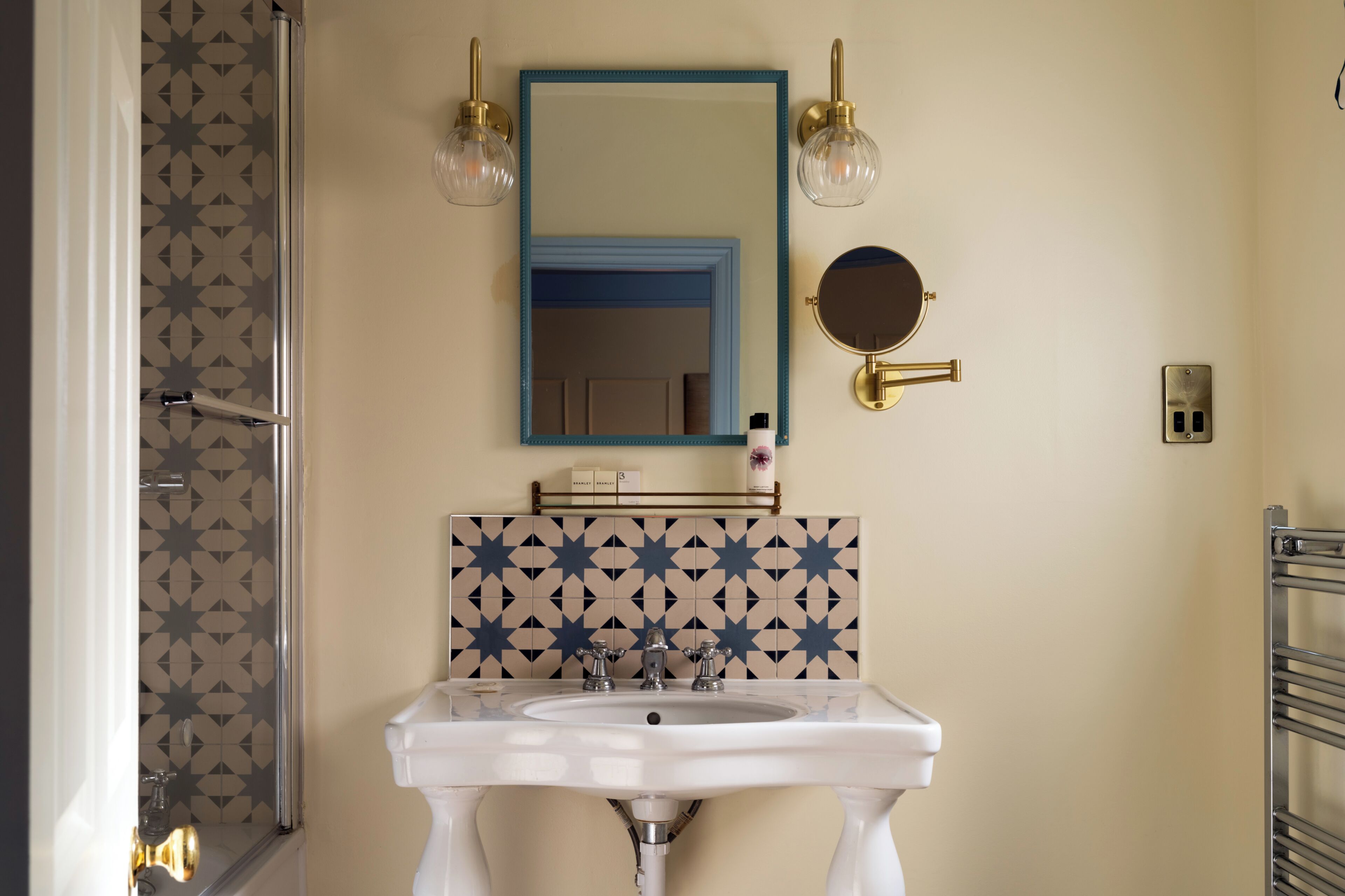 Un baño con un lavamanos blanco, un espejo con marco azul, un espejo redondo y dos apliques de pared.