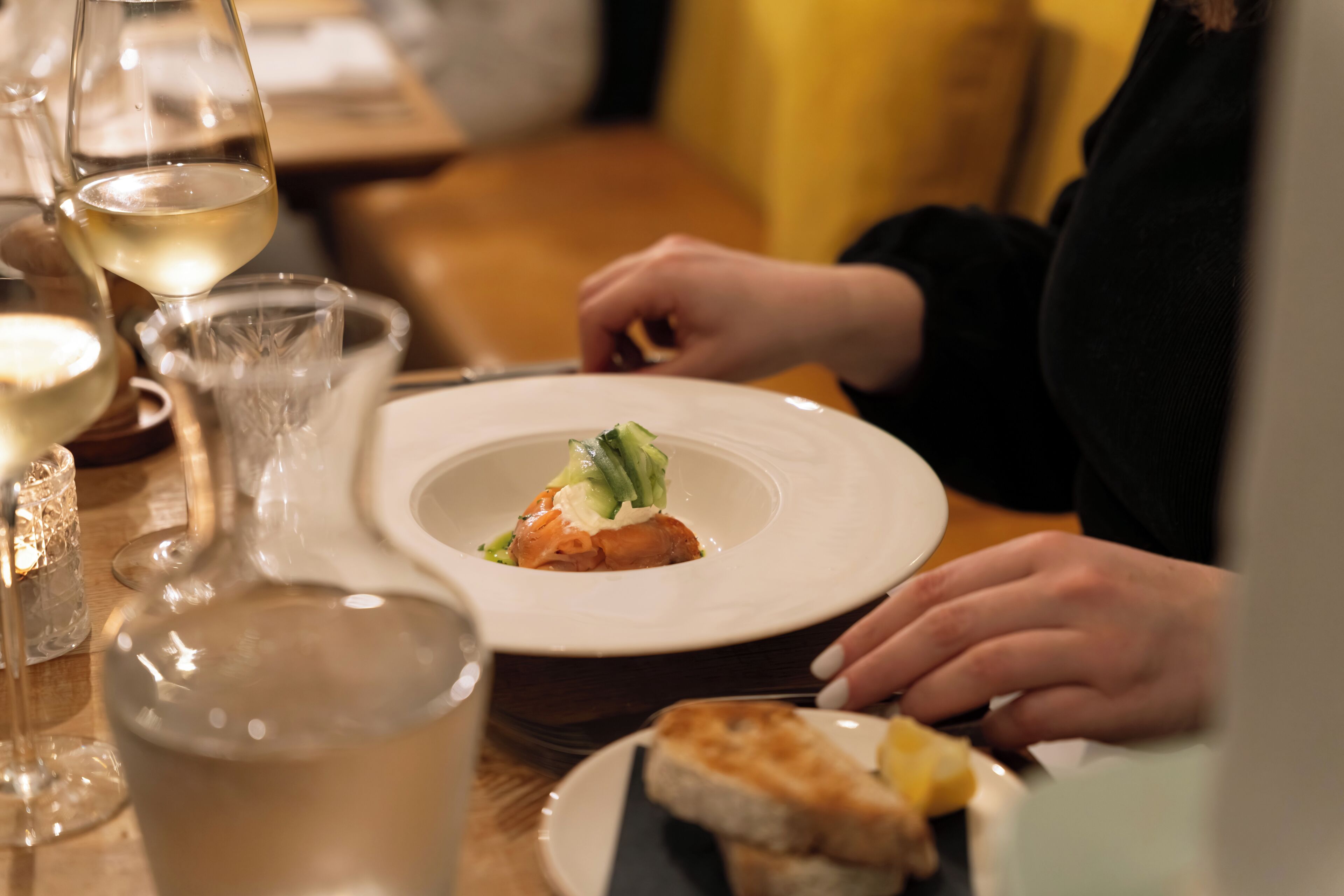 Una mesa de comedor con un plato de comida, una copa de vino blanco y una vela.