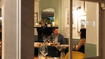 A dining area with tables set for two, a mirror reflecting the room, and a decorative vase on the table.