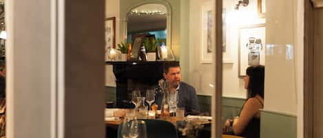 A dining area with tables set for two, a mirror reflecting the room, and a decorative vase on the table.