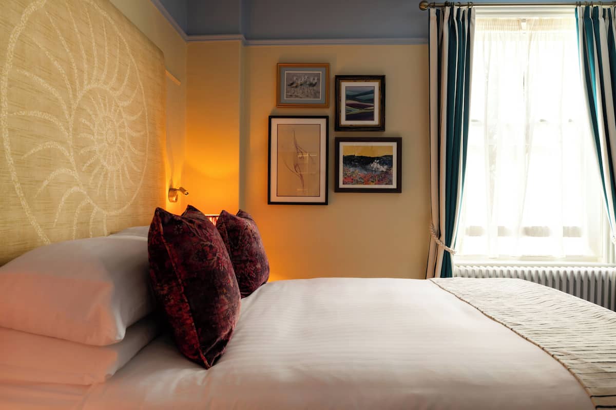 A hotel room with a bed, pillows, wall art, and a window with curtains.
