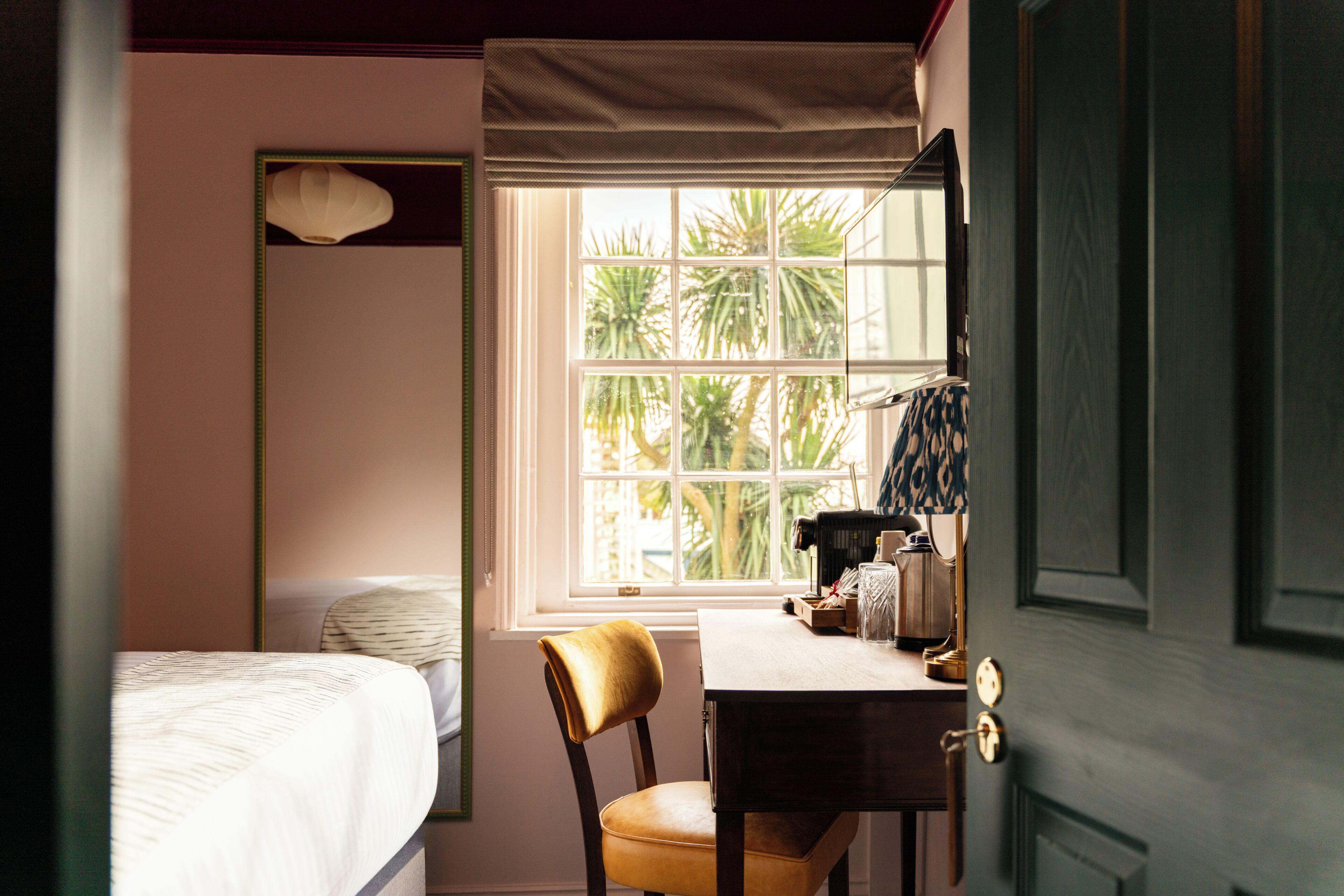 Une chambre à coucher avec un lit, une chaise, un bureau et une fenêtre donnant sur des palmiers.