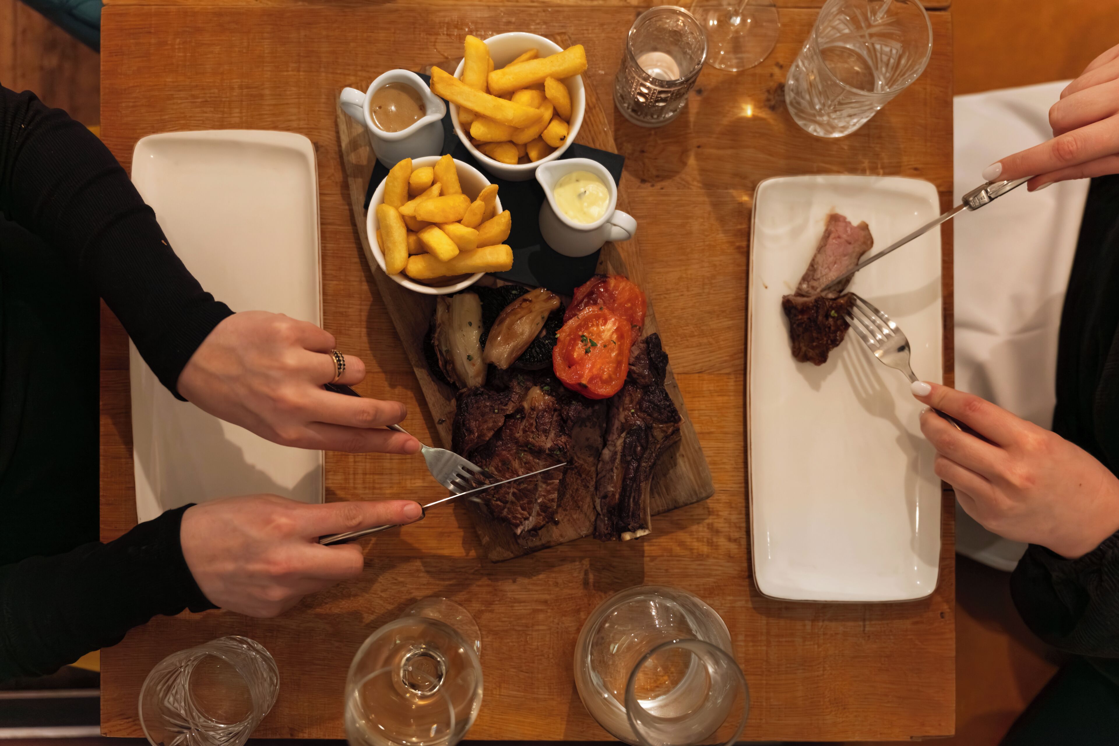 Une table à manger avec une assiette contenant un steak, des frites et une tomate, ainsi que deux verres d’eau et une fourchette.