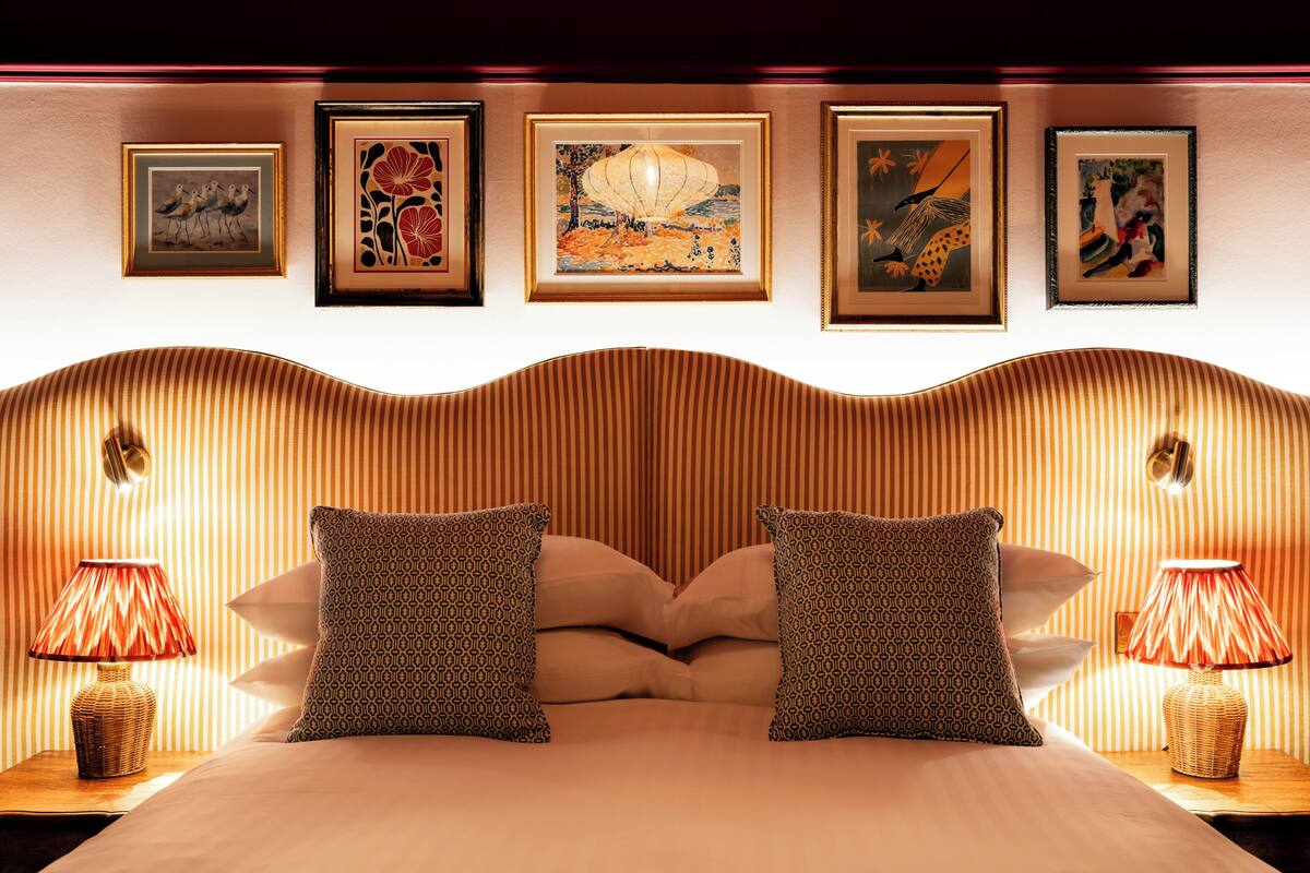 A hotel room with a bed, two nightstands, a wall with framed artwork, and a striped wall design.