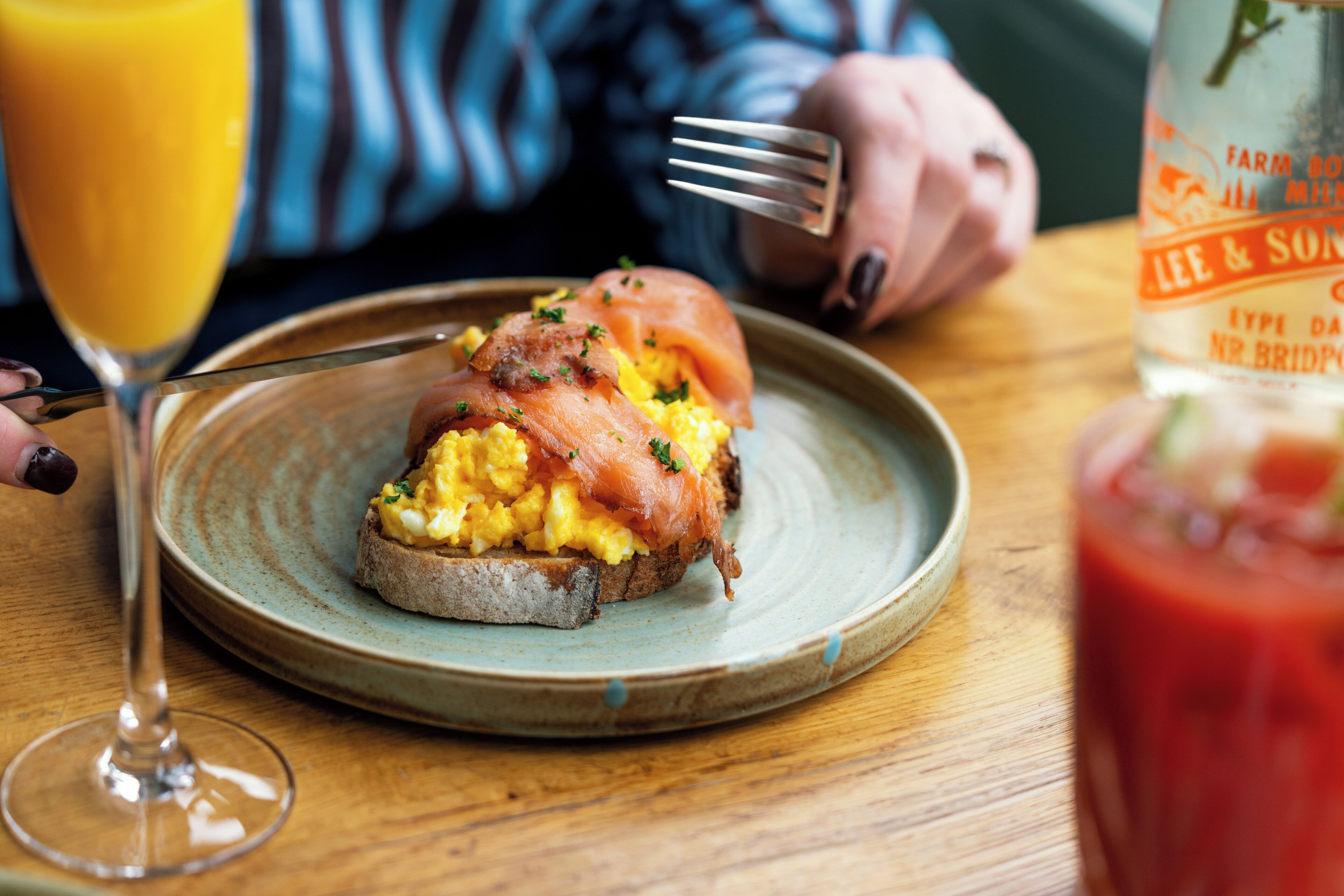 A plate with scrambled eggs and smoked salmon on toast, a glass of orange juice, and a bottle of Farm Boy milk.