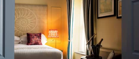A hotel room with a bed, a lamp, curtains, a framed picture, and a bottle on a side table.