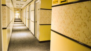 A hotel corridor with doors on both sides, a floral wallpaper pattern on the right wall, and an elevator sign above. - Hotel Sogo Recto (Manila)