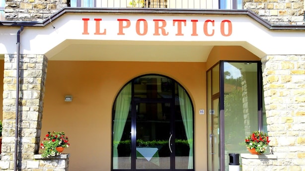 La entrada a IL PORTICO, con fachada de piedra, puertas de cristal y plantas en macetas.