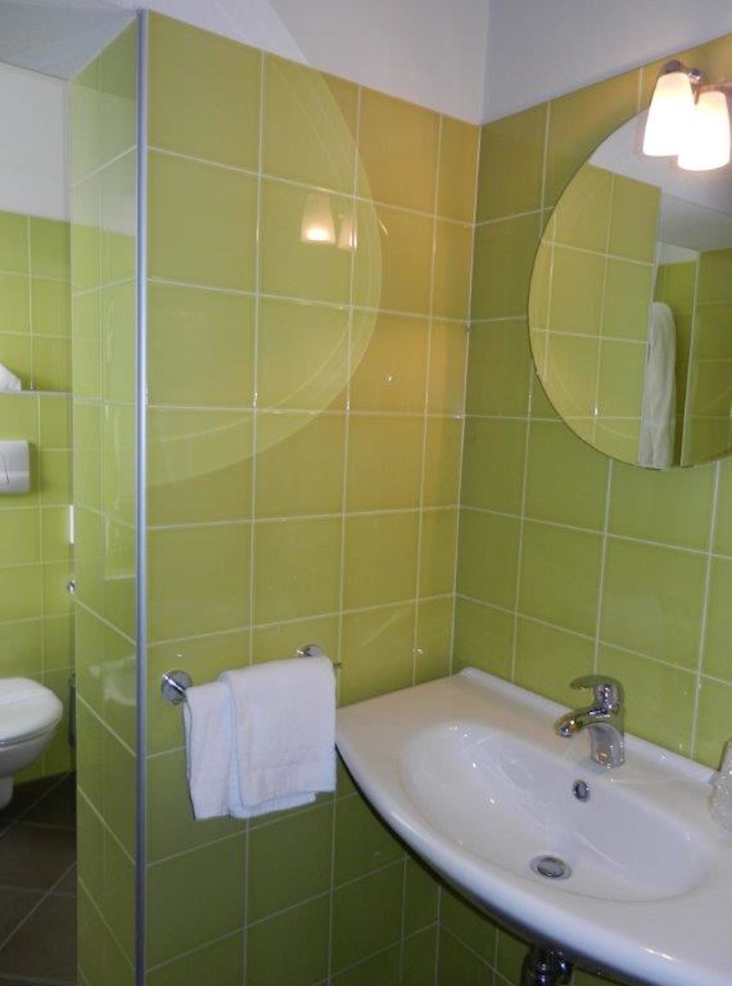 Un baño con azulejos verdes, un lavamanos blanco, un espejo y un perchero para toallas.