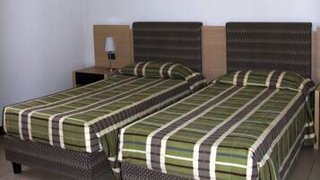 A hotel room with two single beds, a nightstand, a lamp, and a wall-mounted picture.