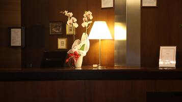 A reception desk with a white vase of flowers, a red ribbon, and a standing lamp.