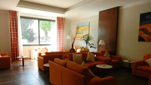 Un moderno vestíbulo de hotel con sofás naranjas, un ventanal con cortinas, un cuadro en la pared y una planta en maceta.